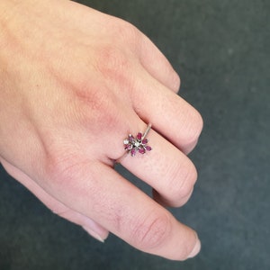 May include: A silver ring with a cluster of small red gemstones and a single white gemstone in the center, shaped like a flower.