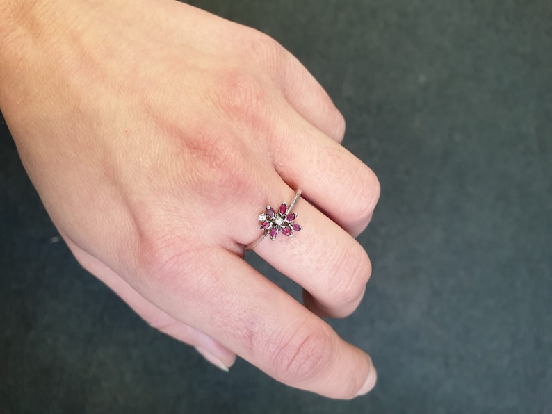 May include: A silver ring with a cluster of small red gemstones and a single white gemstone in the center, shaped like a flower.
