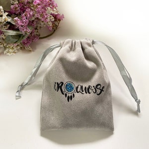 May include: A gray velvet drawstring bag with a blue and white dreamcatcher design and the text "IROQUOISE" printed on the front.