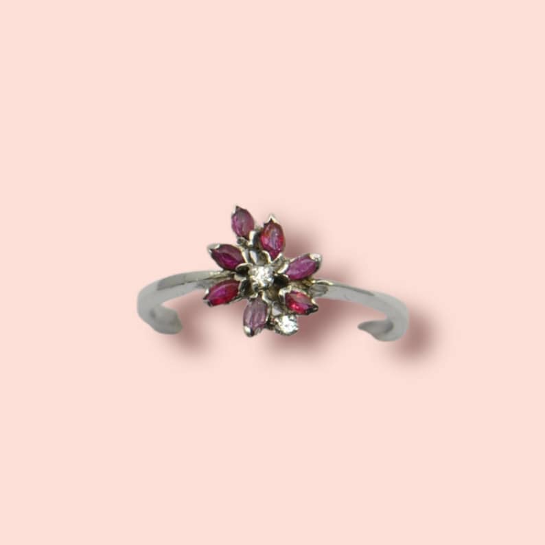 Peut inclure: Une bague en argent avec un motif en forme de fleur orné de pierres précieuses roses et blanches.