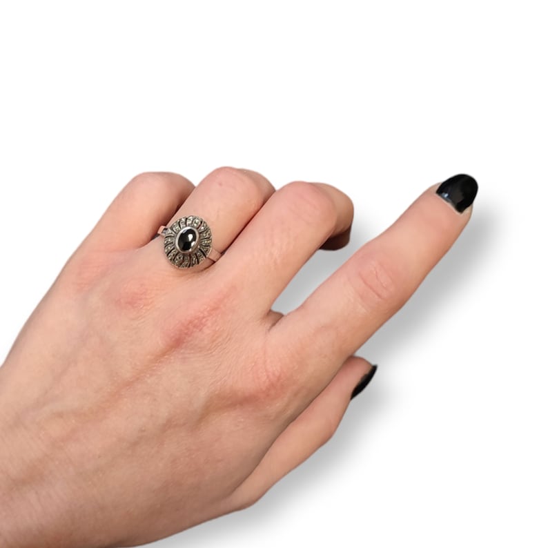 May include: A silver ring with a black oval gemstone surrounded by a cluster of smaller stones.