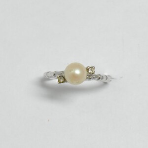 May include: A silver ring with a white pearl and two small clear stones.