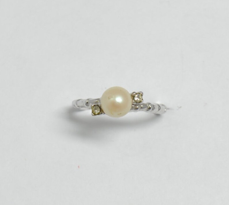 May include: A silver ring with a white pearl and two small clear stones.