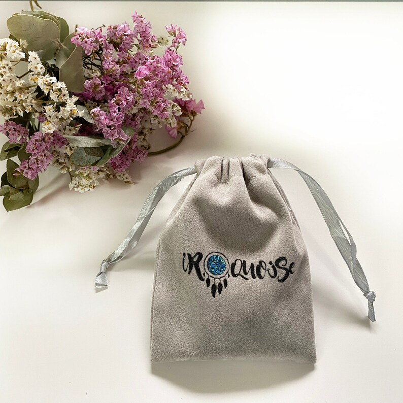 May include: A gray velvet pouch with a drawstring closure and a blue and black dreamcatcher design with the text "IROQUOISE" printed on it.