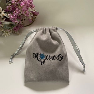 May include: A gray velvet pouch with a drawstring closure. The pouch has a black logo that says "IROQUOISE" with a blue and white dreamcatcher design.