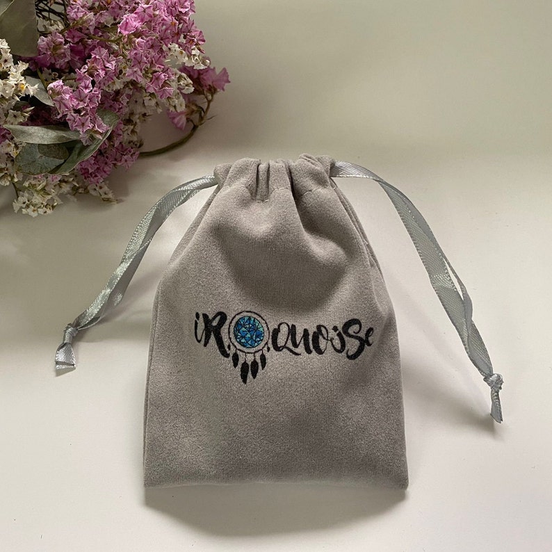 May include: A gray velvet pouch with a drawstring closure. The pouch has a black logo that says "IROQUOISE" with a blue and white dreamcatcher design.