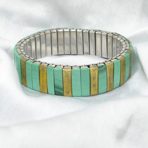May include: A green and gold stretchy bracelet with a metal band.