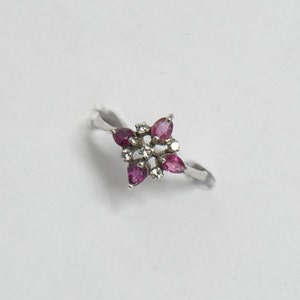 May include: A silver ring with a flower-shaped design featuring pink gemstones and small white diamonds.