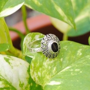 May include: A silver ring with a black oval stone surrounded by a detailed marquetry design.