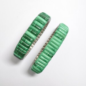 May include: Two green malachite stone bracelets with a silver metal band.