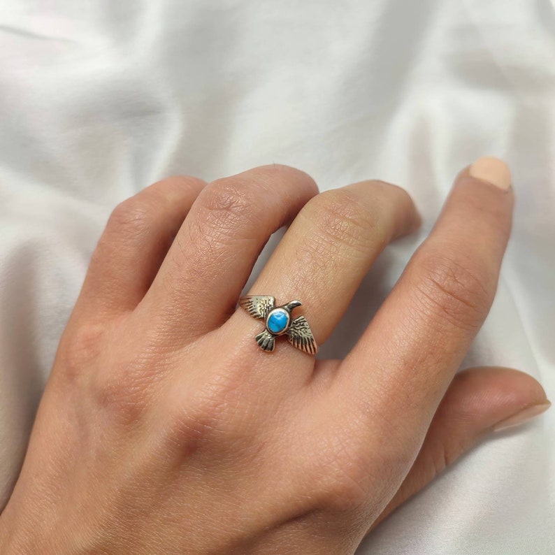 May include: A silver ring featuring a turquoise stone set in the shape of a bird. The bird is depicted in flight with its wings outstretched.