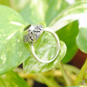 May include: A silver ring with a black gemstone set in a marcasite design. The ring is on a green leaf.
