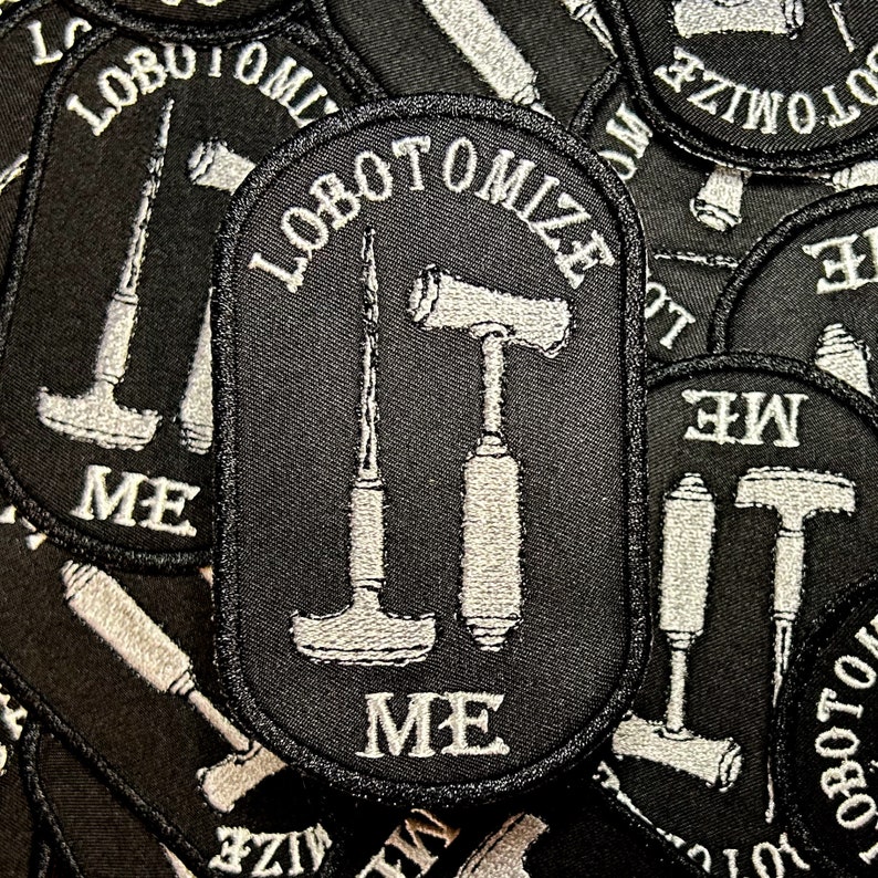 May include: Close-up of a black embroidered patch with white stitching. The patch features three tools: a hammer, a chisel, and a screwdriver. The text "lobotomize me" is written in white on the patch.