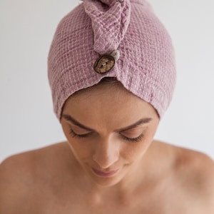 Pu&ograve; includere: Un turbante per capelli in tessuto a nido d'ape rosa con un bottone in legno. Il turbante &egrave; indossato sulla testa di una persona.