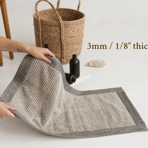 May include: A gray and white bath mat with a textured surface and a gray border. The mat is 3mm / 1/8" thick.