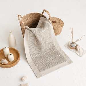 May include: A woven basket with a lid, a white bath mat, and two small white ceramic vases on a wooden tray. The items are arranged on a white surface.