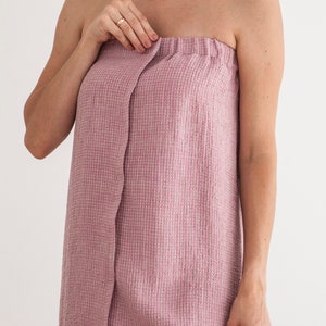 Pu&ograve; includere: Un accappatoio rosa in tessuto a nido d'ape con uno stile avvolgente e una chiusura a bottone singolo.