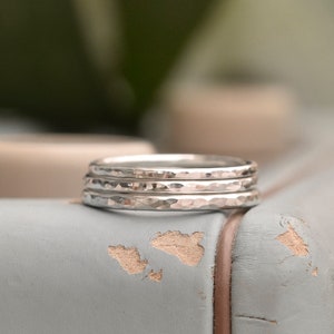 May include: Three silver hammered stacking rings on a light blue surface.