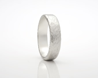 May include: A silver ring with a textured, hammered finish. The ring is wide and has a rounded profile.