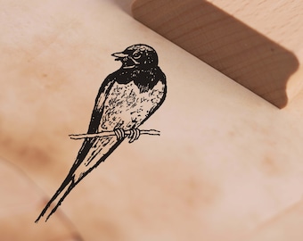 May include: A black and white illustration of a bird perched on a branch. The bird has a long tail and a small beak. The illustration is on a white background.