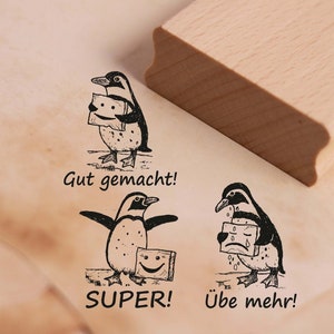 Könnte beinhalten: Drei schwarz-weiße Pinguin-Illustrationen auf einer Holzoberfläche. Die Pinguine halten Schilder mit verschiedenen Gesichtsausdrücken. Der Text auf den Schildern lautet "Gut gemacht!" "Super!" und "Übe mehr!"
