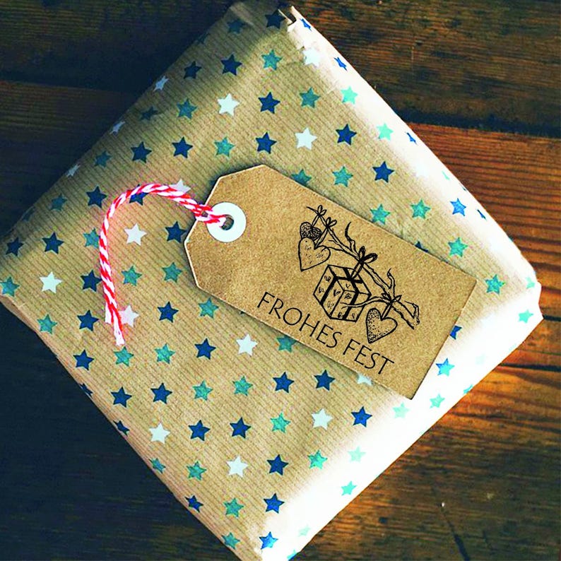 May include: A brown paper gift bag with a blue and white star pattern. A brown tag with a white circle and the text "Frohes Fest" is attached to the bag.