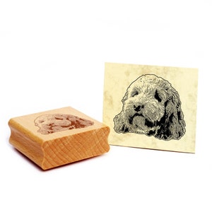 Könnte beinhalten: Ein Holz-Stempel mit einer Schwarzweiß-Illustration eines Hundekopfes. Der Hund hat lockiges Haar und schaut direkt auf den Betrachter.