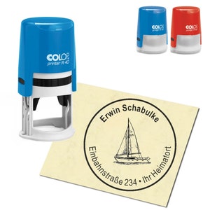 May include: A blue and red self-inking stamp with the text "COLOP printer R 40" on the side. The stamp is used to create a round imprint with the text "Erwin Schabulke Einbahnstraße 234 Ihr Heimatort" and a sailboat graphic.