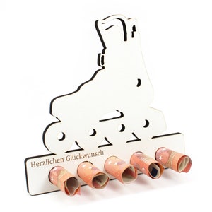 Peut inclure: Porte-monnaie en bois blanc en forme de patin à roulettes avec le texte "Herzlichen Glückwunsch" en bas. Le porte-monnaie a six fentes pour les billets enroulés.