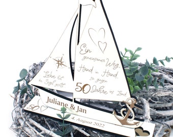 May include: A wooden sailboat with a compass, anchor, and hearts. The text reads "Ein gemeinsamer Weg. Hand in Hand. So gingen 50 Jahre ins Land." and "Juliane & Jan 4. August 2022".