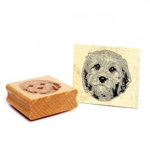 Op de afbeelding: Een houten rubberen stempel met een zwart-witte illustratie van een hondenkop. De hond heeft krullend haar en kijkt recht in de camera.