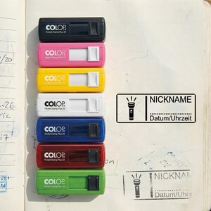 May include: A collection of COLOP Pocket Stamp Plus 20 stamps in various colors: black, pink, yellow, white, blue, red, and green. Each stamp has a white sliding mechanism. A rectangular stamp with a flashlight icon and the words "NICKNAME" and "Datum/Uhrzeit" is also shown.