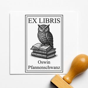 Könnte beinhalten: Schwarz-weißer Stempel mit dem Text "EX LIBRIS" und einer Illustration einer Eule auf einem Bücherstapel. Der Name "Oswin Pfannenschwanz" ist darunter gedruckt. Ein Holzstempelgriff ist im Vordergrund zu sehen.