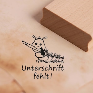 Op de afbeelding: Een zwart-witte rubberen stempel met een cartoonrups die een pen vasthoudt en de tekst "Unterschrift fehlt!" wat "Handtekening ontbreekt!" betekent in het Nederlands.