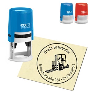 Könnte beinhalten: Ein blauer und roter Stempel mit Selbsttinte und dem Text "COLOP printer R 40" an der Seite. Der Stempel wird verwendet, um einen runden Abdruck mit dem Text "Erwin Schabulke Einbahnstraße 234 Ihr Heimator" und einer Grafik eines Gabelstaplers zu erstellen.