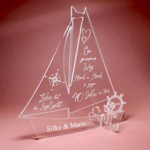 Könnte beinhalten: Transparente Segelboot-Dekoration aus Acryl mit graviertem Text und nautischen Elementen. Mit Kompassrose, Herzen und den Namen "Silke & Mario". Enthält den Text "40 Jahre ins Land" und das Jahr "2025."