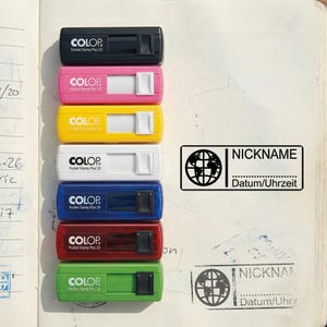 Könnte beinhalten: Eine Auswahl an COLOP Pocket Stamp Plus 20 Stempeln in Schwarz, Pink, Gelb, Weiß, Blau, Rot und Grün. Jeder Stempel hat einen weißen Schiebemechanismus. Ein separater Stempel zeigt eine Weltkugel-Grafik mit den Worten "NICKNAME" und "Datum/Uhrzeit".
