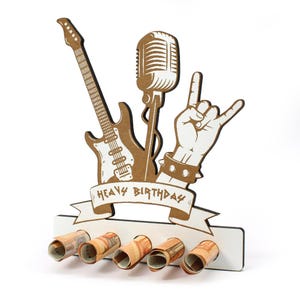 Könnte beinhalten: Ein weiß-brauner Geburtstagskartenhalter aus Holz mit Rock'n'Roll-Motiv. Das Design umfasst eine Gitarre, ein Mikrofon und eine Hand, die das Rock-Zeichen macht. Die Worte "Heavy Birthday" stehen auf einem Banner. Fünf gerollte Geldscheine befinden sich im Kartenhalter.