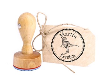 May include: Wooden stamp with a dinosaur design and the text "Martin Kersten" in a circle. The stamp is on a brown paper tag with twine.