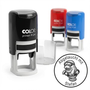 Könnte beinhalten: Ein schwarzer und grauer COLOP printer R 24 Stempel mit einer transparenten Kunststoffabdeckung. Zwei weitere Stempel in Rot und Blau befinden sich im Hintergrund. Ein runder Stempel mit einem Cartoon-Manati mit Brille und Schwimmring ist ebenfalls zu sehen.