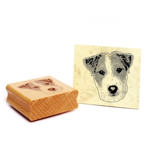 Könnte beinhalten: Ein Holz-Stempel mit einer Schwarzweiß-Illustration eines Jack-Russell-Terrier-Hunde-Kopfes. Der Stempel befindet sich auf einer weißen Oberfläche neben einer Karte mit dem gleichen Bild.