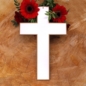 Peut inclure: Une croix en bois blanc au design simple, entourée de fleurs rouges. La croix est sur un fond en bois brun.