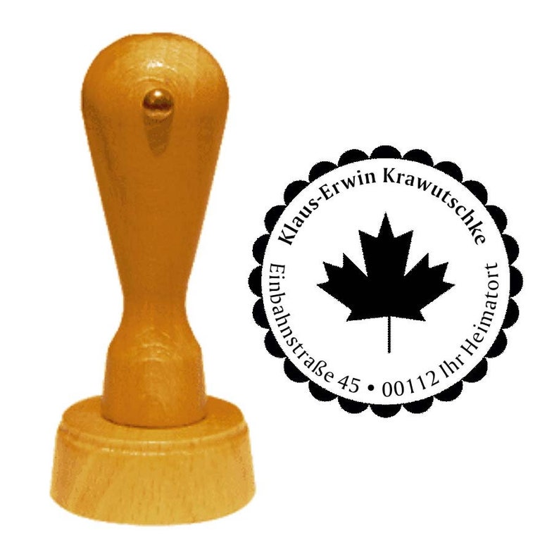 May include: A wooden self-inking stamp with a black and white circular design. The design features a maple leaf, the text "Klaus-Erwin Krawutschke", "Einbahnstra&szlig;e 45", and "00112 Ihr Heimatort".