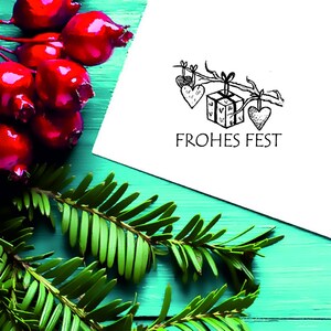 May include: A white card with a black and white illustration of a gift box with hearts hanging from a branch. The text "FROHES FEST" is printed below the illustration.