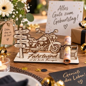 Könnte beinhalten: Ein dekorativer Holzaufsteller mit einer lasergeschnittenen Motorradfigur und einem Wegweiser mit den Wörtern Freiheit, Abenteuer, Kurven und Glück. Der Sockel trägt den Text Fahrtwind ist die beste Therapie und einen Halter für einen Geldschein.