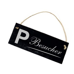 Puede incluir: Un letrero de pizarra negra con texto blanco que dice "P Besucher" colgado de una cuerda de yute.