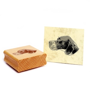 Op de afbeelding: Een houten stempel met een illustratie van een hondenhoofd en een bijpassende afdruk op een kaart. De stempel is rechthoekig met een gebogen handvat. De hondenillustratie is in zwart en wit.