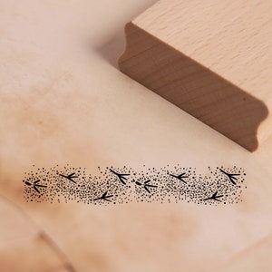 Könnte beinhalten: Ein Stempel aus Holz mit einem Design aus einer Reihe kleiner Vogelabdrücke. Der Stempel ist aus hellem Holz gefertigt und hat eine rechteckige Form.