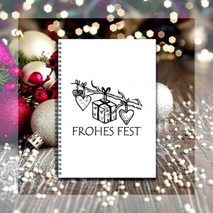 May include: A white spiral bound notebook with a black and white illustration of a gift box and hearts hanging from a branch. The text "Frohes Fest" is printed below the illustration.