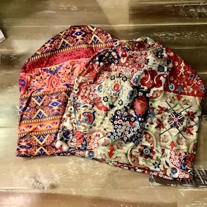 May include: Two slouchy beanies featuring vibrant, multi-colored patterns. The left beanie displays a geometric design in shades of orange, red, and blue. The right beanie showcases a complex floral and tile-inspired print in red, blue, and cream.